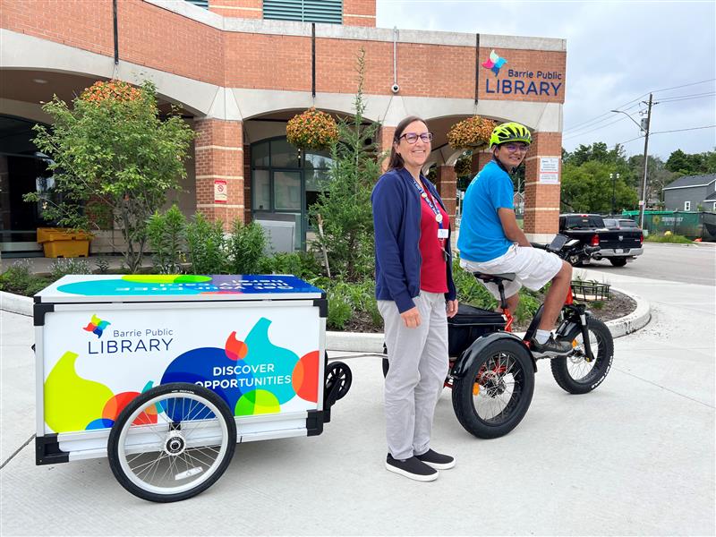 BPL staff member sits on e-Trike with trailer in front of Downtown Library